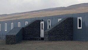 Un bâtiment à l’extérieur gris, doté d’une porte centrale et de nombreuses fenêtres.