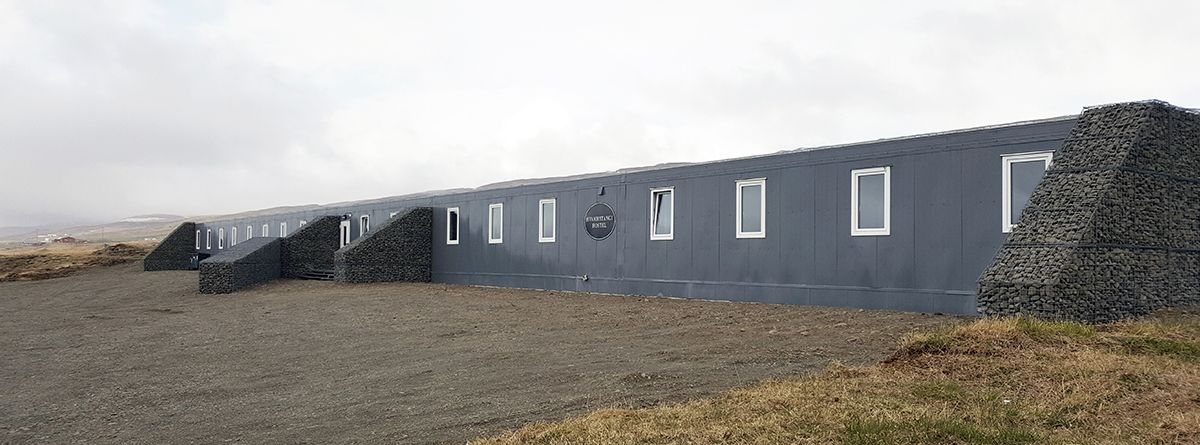 A long, narrow building with multiple windows and a stone structure on one side.