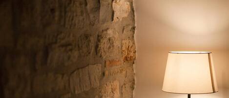 A lamp with a beige shade against a textured stone wall.