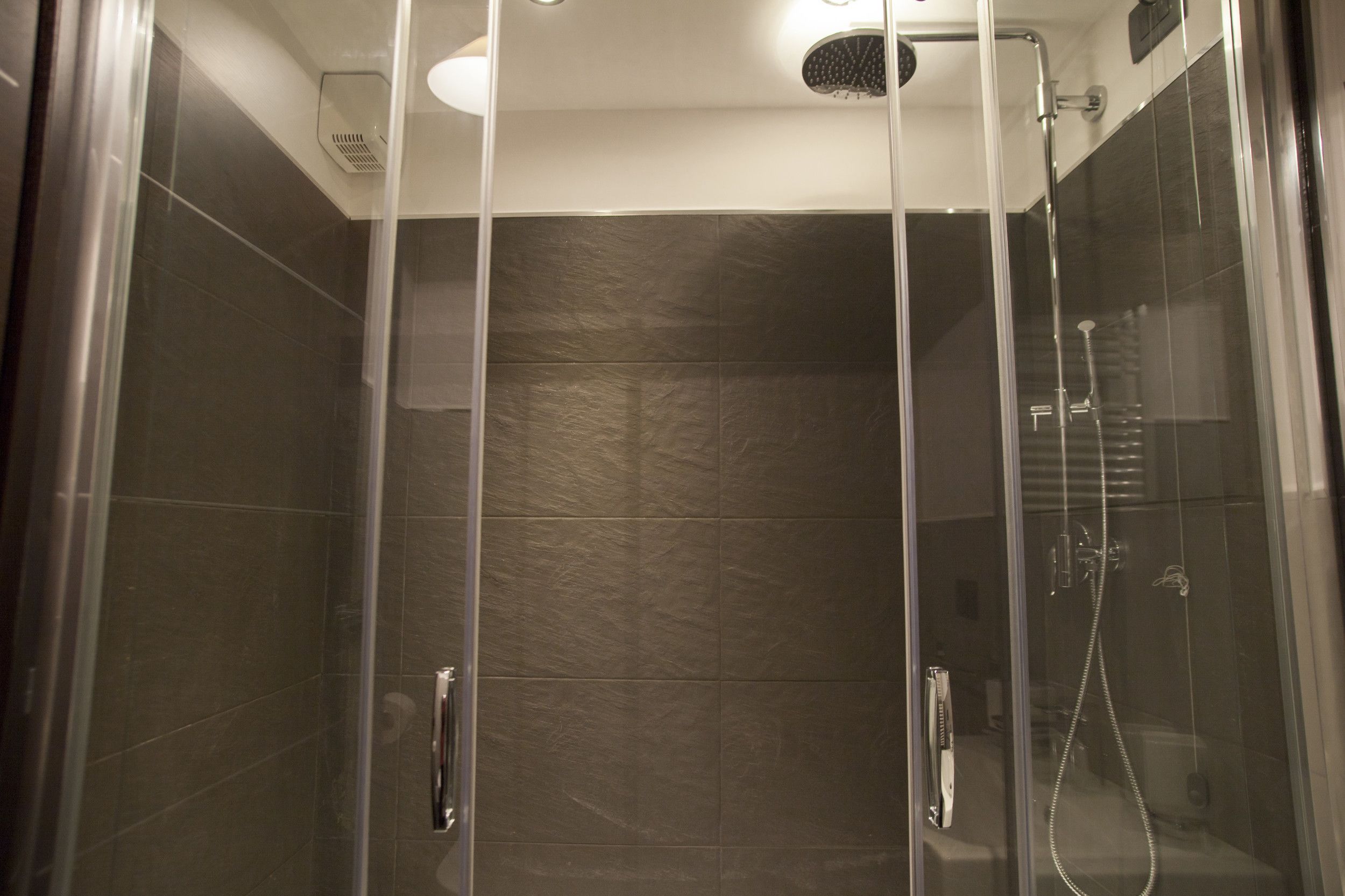 A glass-enclosed shower stall with a handheld showerhead and a handheld shower attachment.