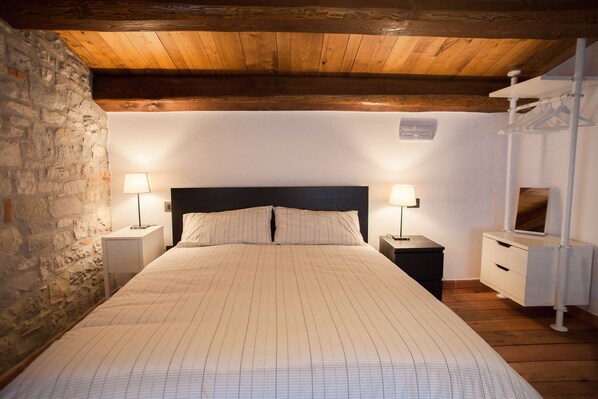 Un dormitorio con una cama grande, dos mesitas de noche, un aparador y techo de madera, además de una pared de piedra.