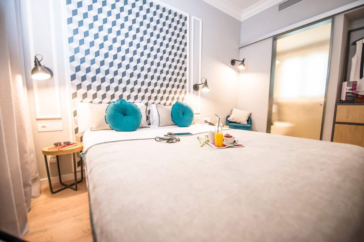 A neatly made bed with a geometric patterned headboard, a bedside table with a lamp, and a closet with a sliding door.