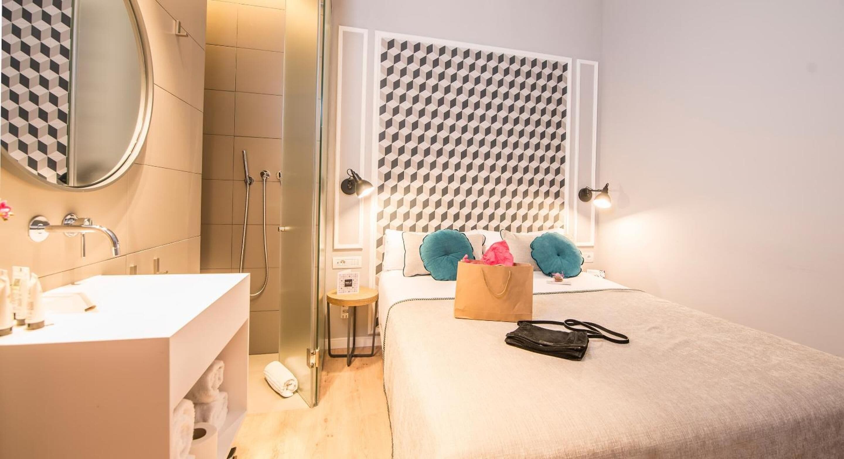 Een moderne badkamer met een grote spiegel, een wastafel en een douche. Er staat een bed met een gestreept hoofdeinde en kussens.