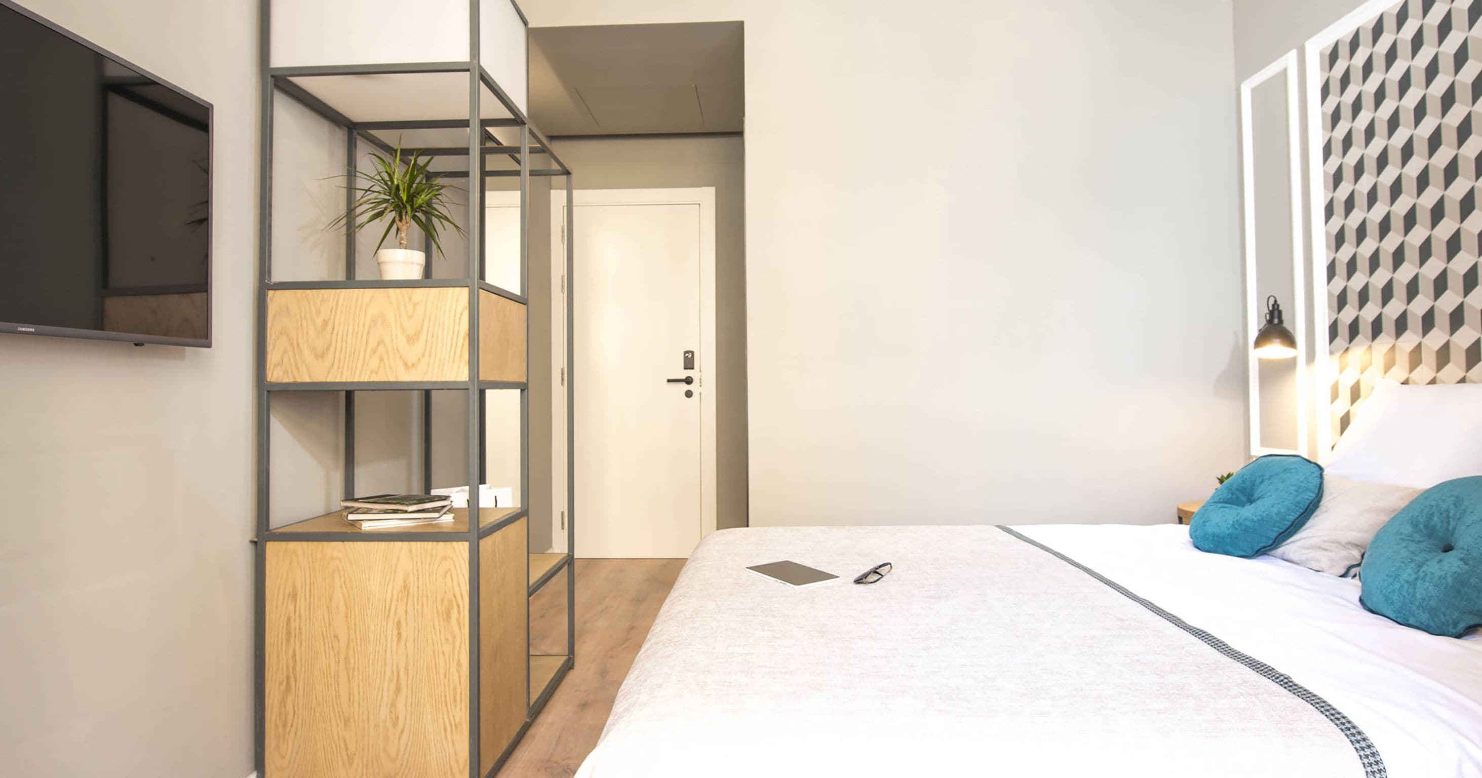 Una camera da letto moderna con un letto, una libreria a muro in legno, una pianta in vaso e una testiera imbottita a motivi geometrici.