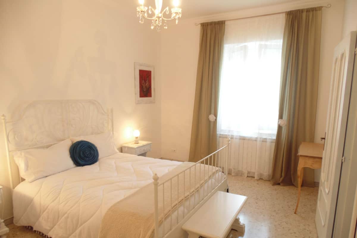 A bedroom with a bed, bedside table, lamp, and a small bench.