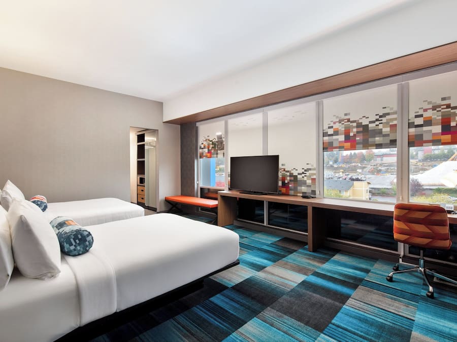 A hotel room with a large window, a bed, a desk with a computer, and a chair.