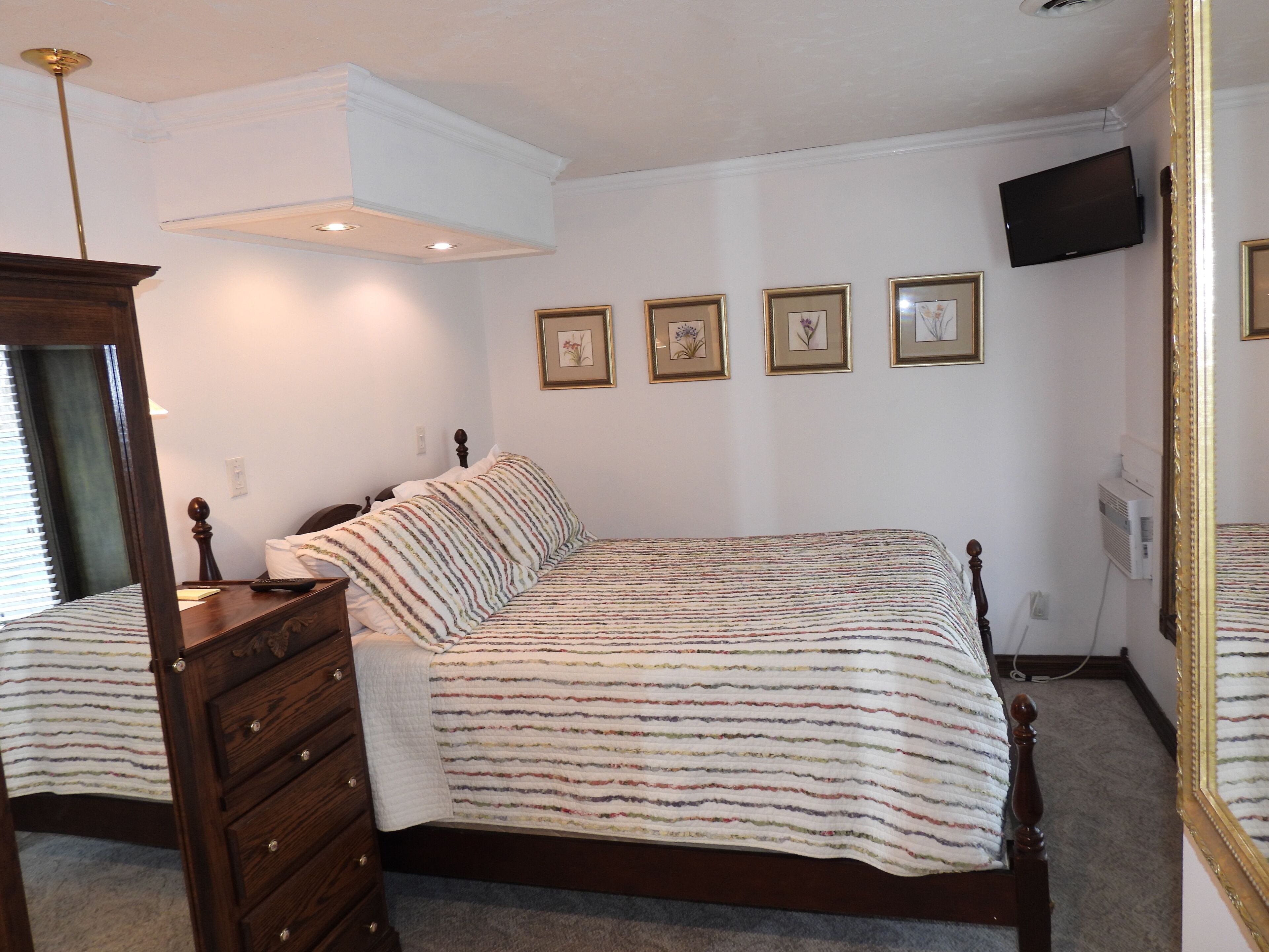 A bedroom with a bed, dresser, and a television on the wall.