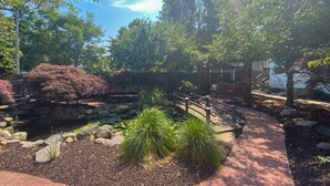 Un jardin aménagé avec un mur en pierre, un pont en bois et une grande variété de plantes.