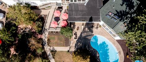 An aerial view of a residential property with a swimming pool, patio area with umbrellas, and a covered deck.