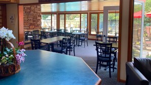 Un restaurant avec des tables et des chaises en bois, un mur en pierre et une enseigne sur laquelle on peut lire : « Asseyez-vous, parlez longtemps, riez souvent. »