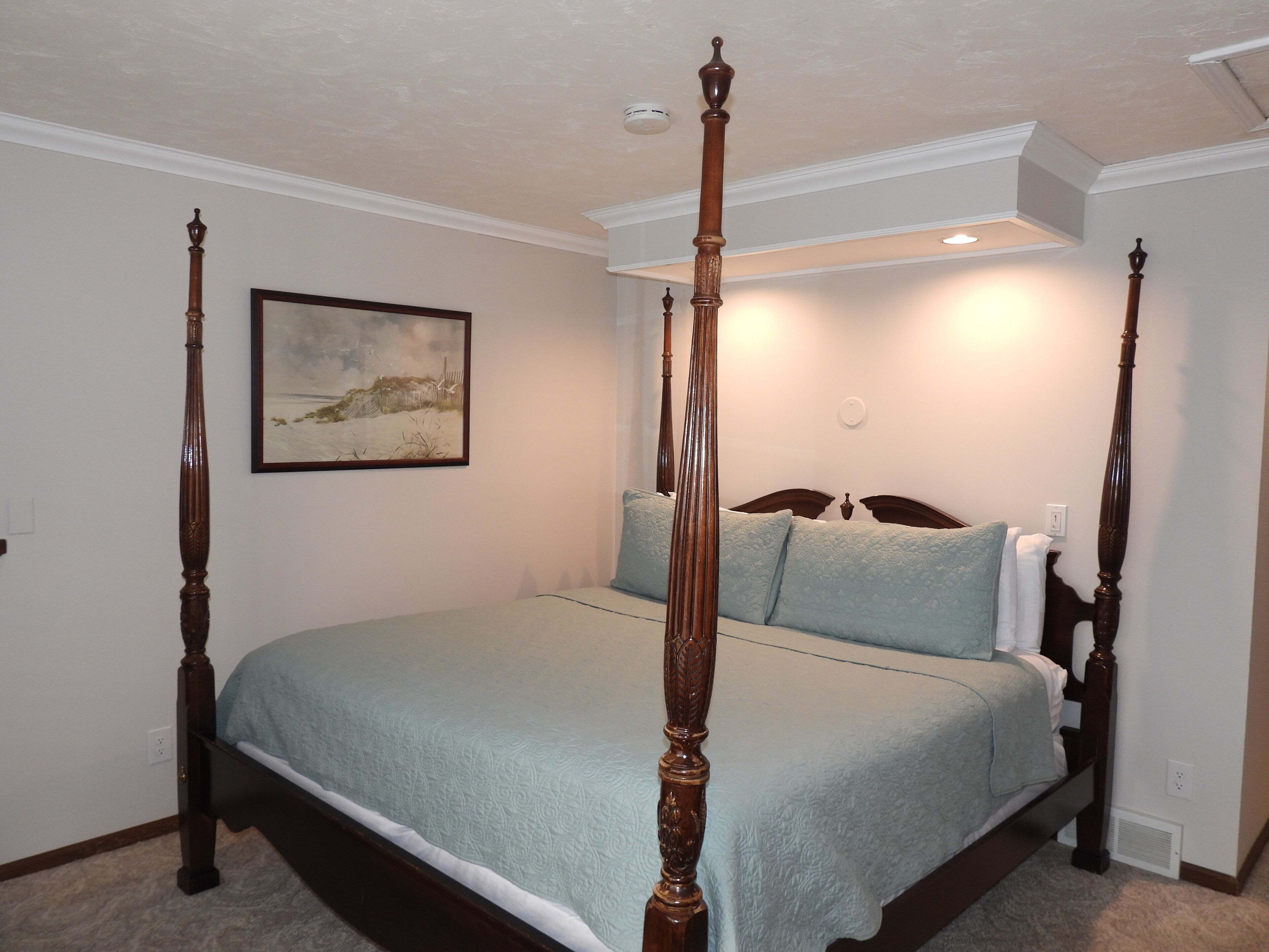 A four-poster bed with a headboard, a painting on the wall, and a ceiling light.