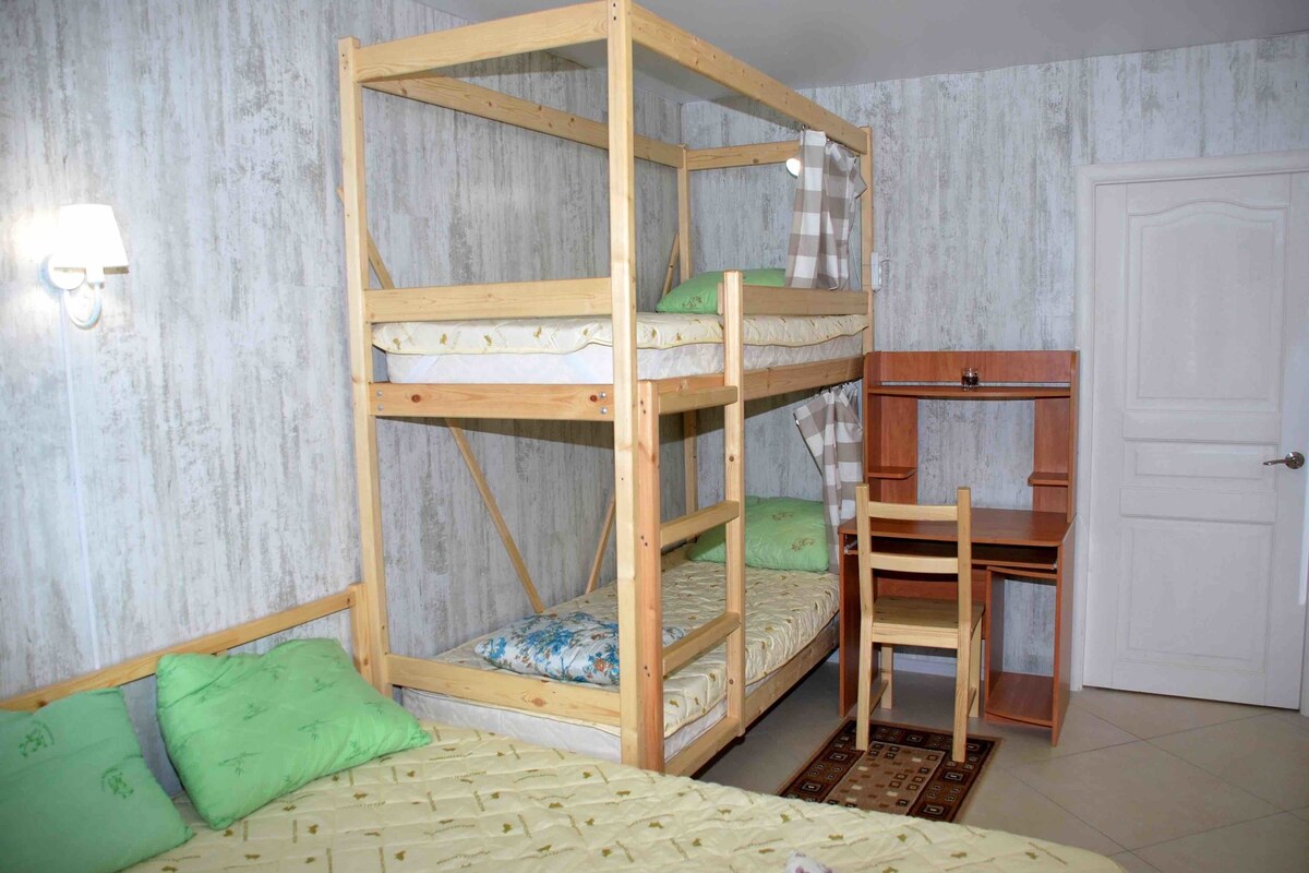 A bunk bed with a desk and chair, a white door, and a wall-mounted light fixture.
