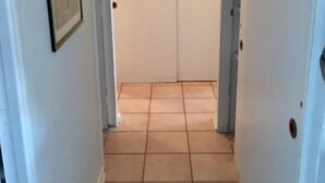 A narrow hallway with white walls and a tiled floor leading to a closed door. - Departamento Puerto Velero Angelica (Coquimbo)