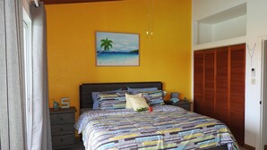 A bedroom with a bed, a nightstand, a painting of a beach scene, and a wooden closet.