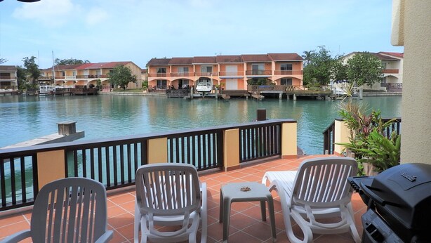 A terrace with two chairs and a grill, overlooking a calm water body with buildings in the background.