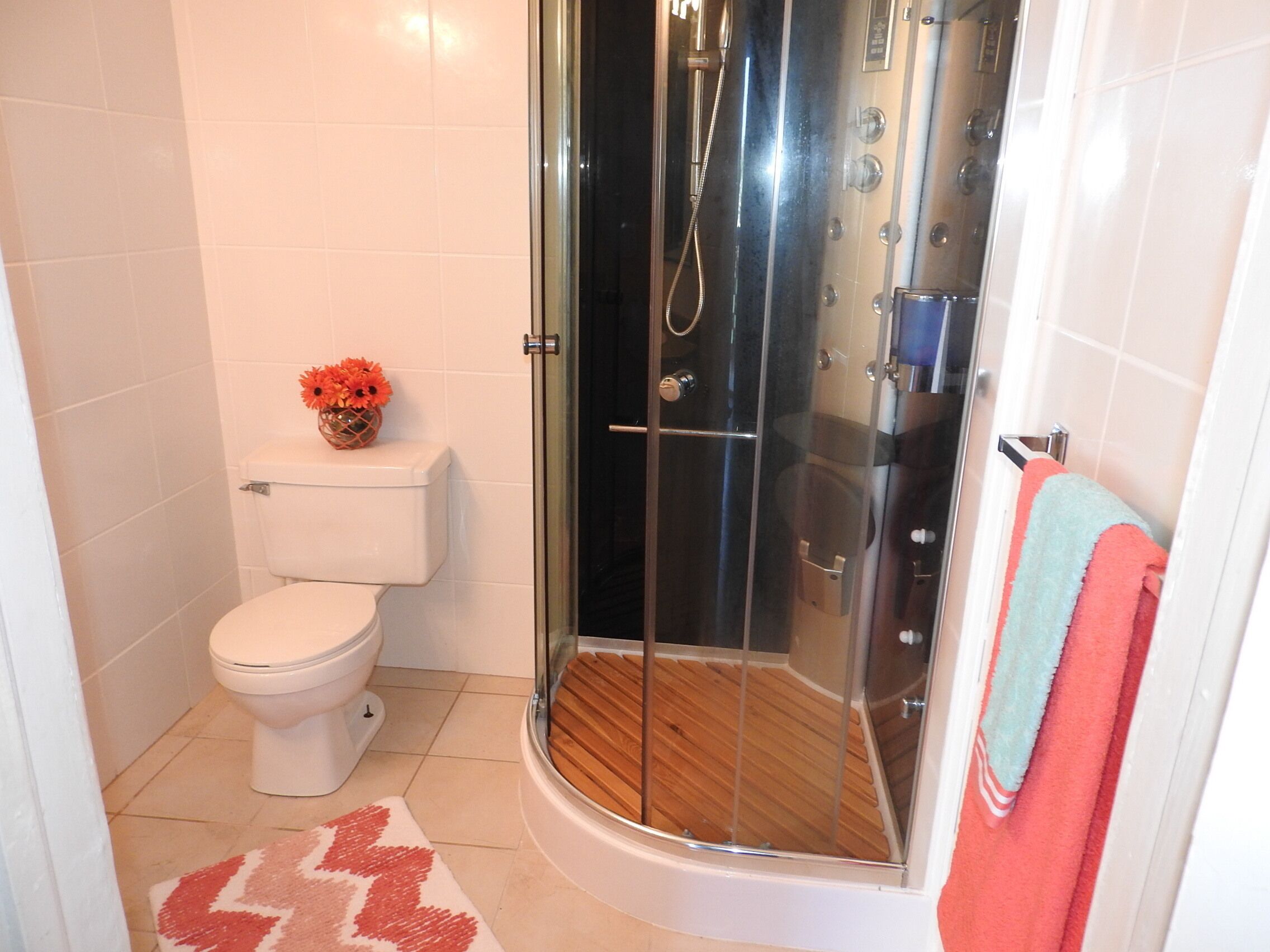 Un baño con inodoro, ducha con mampara de vidrio y piso de madera.