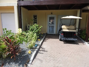 A covered outdoor area with a golf cart, a door labeled 'E', and a garden with various plants.
