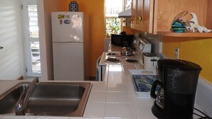A compact kitchen with a refrigerator, stove, sink, and a coffee maker.