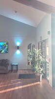 Un salón con un sofá, una mesita y un televisor montado en la pared. Hay dos lámparas de pared y una planta grande en maceta.