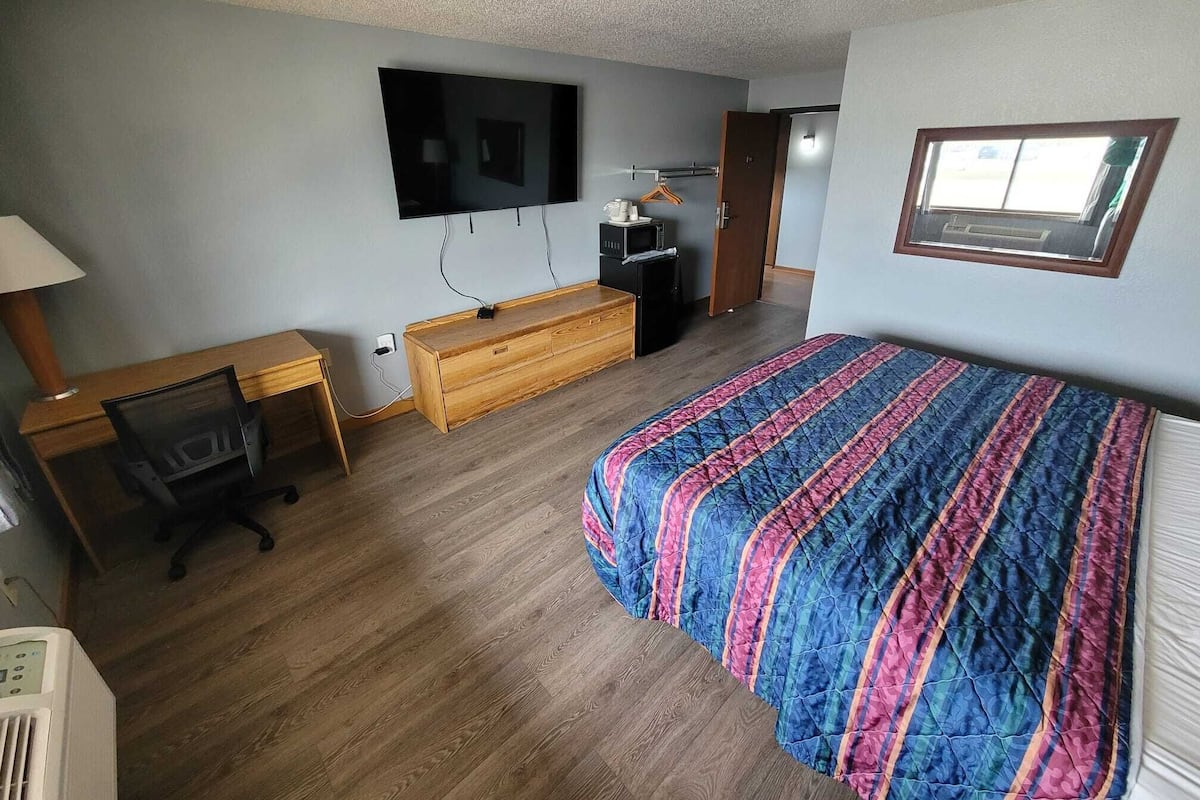 A bedroom with a bed, desk, chair, TV, and a window.