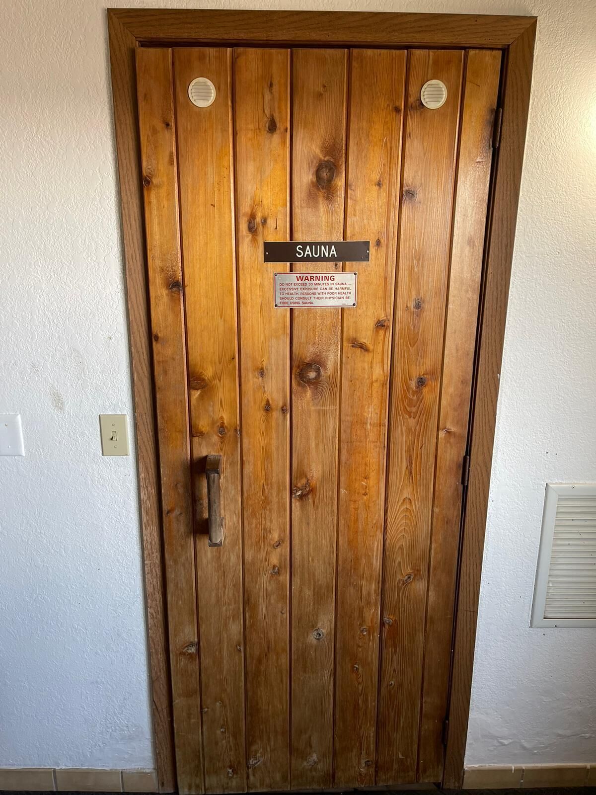 A wooden door labeled "SAUNA" with a warning sign about health risks from excessive use.