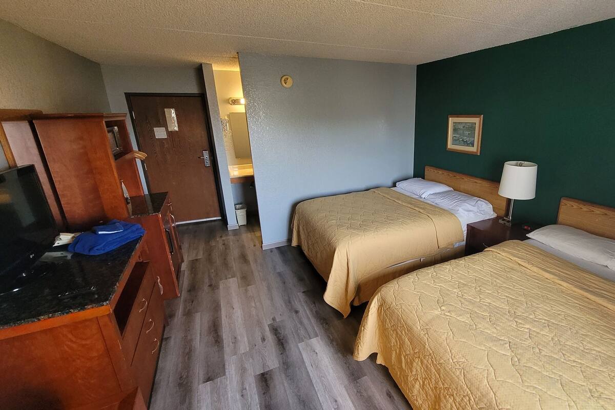 A hotel room with two beds, a television, a desk, and a bathroom visible through an open door.