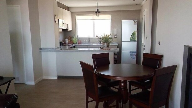 A compact kitchen with a dining table and chairs, a refrigerator, and a window providing natural light.
