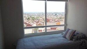 A bedroom with a large window offering a view of a residential area with multiple houses.