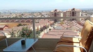 A balcony with a view of a cityscape, including residential buildings and distant mountains.
