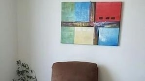 Un soggiorno con una poltrona marrone, un tavolino rotondo, una pianta in vaso e un quadro astratto dai colori vivaci appeso alla parete.