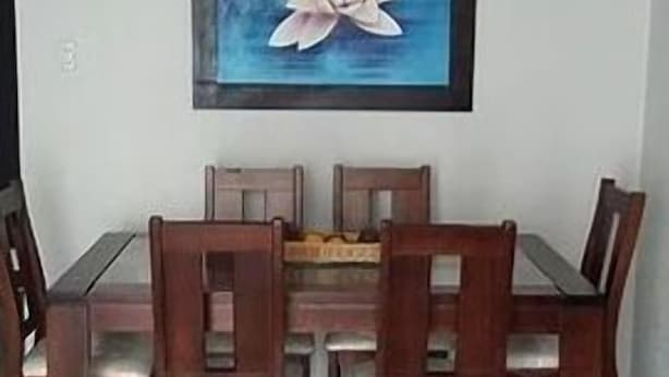 Zona pranzo con tavolo e sedie in legno, un quadro incorniciato raffigurante un fiore di loto e una lampada a sospensione bianca.