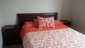 Un letto rifatto con cura, con una coperta a motivi e due cuscini, uno con un disegno floreale.