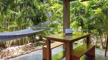 A hammock, a wooden table with a laptop, and lush greenery in a serene outdoor setting.