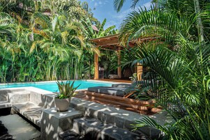 Un área de piscina con terraza de madera, escalones de piedra y exuberante vegetación tropical.