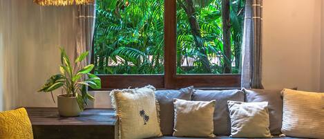 Una habitación con sofá, una planta en maceta y ventana con vistas a follaje.