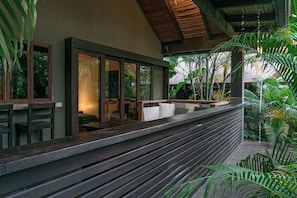 Una terraza de madera con un banco, rodeada de exuberante vegetación tropical.