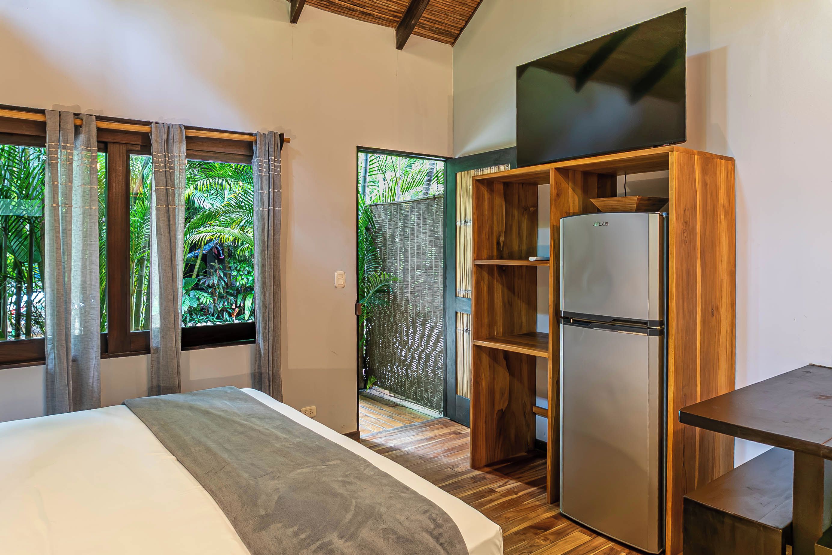 Quarto com cama, guarda-roupa de madeira, frigorífico e janela com cortinas.