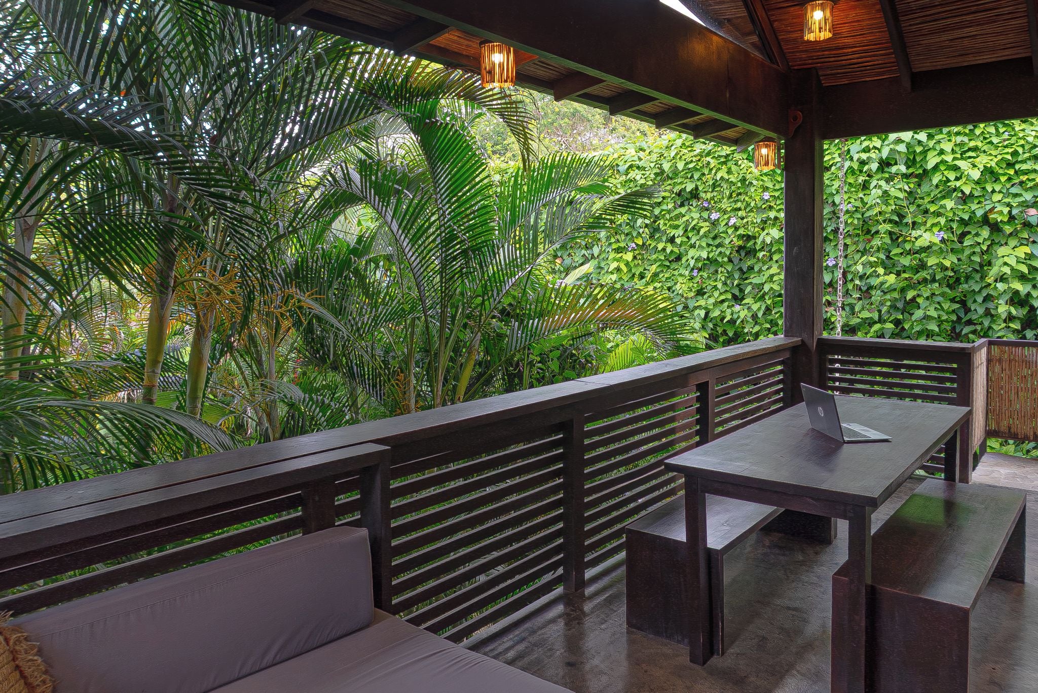 An outdoor seating area with wooden benches and tables, surrounded by lush greenery.