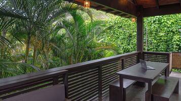 An outdoor seating area with wooden benches and tables, surrounded by lush greenery.