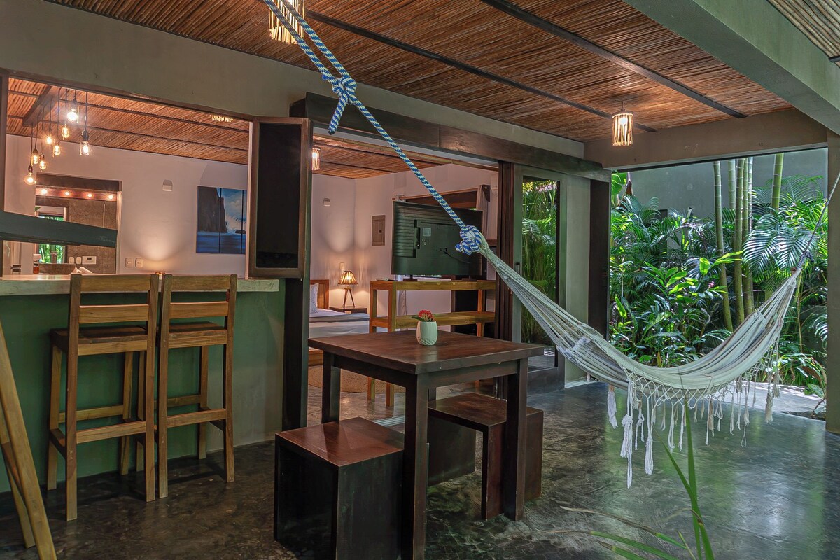 A modern interior with a dining area, a hammock, and a view of lush greenery outside.