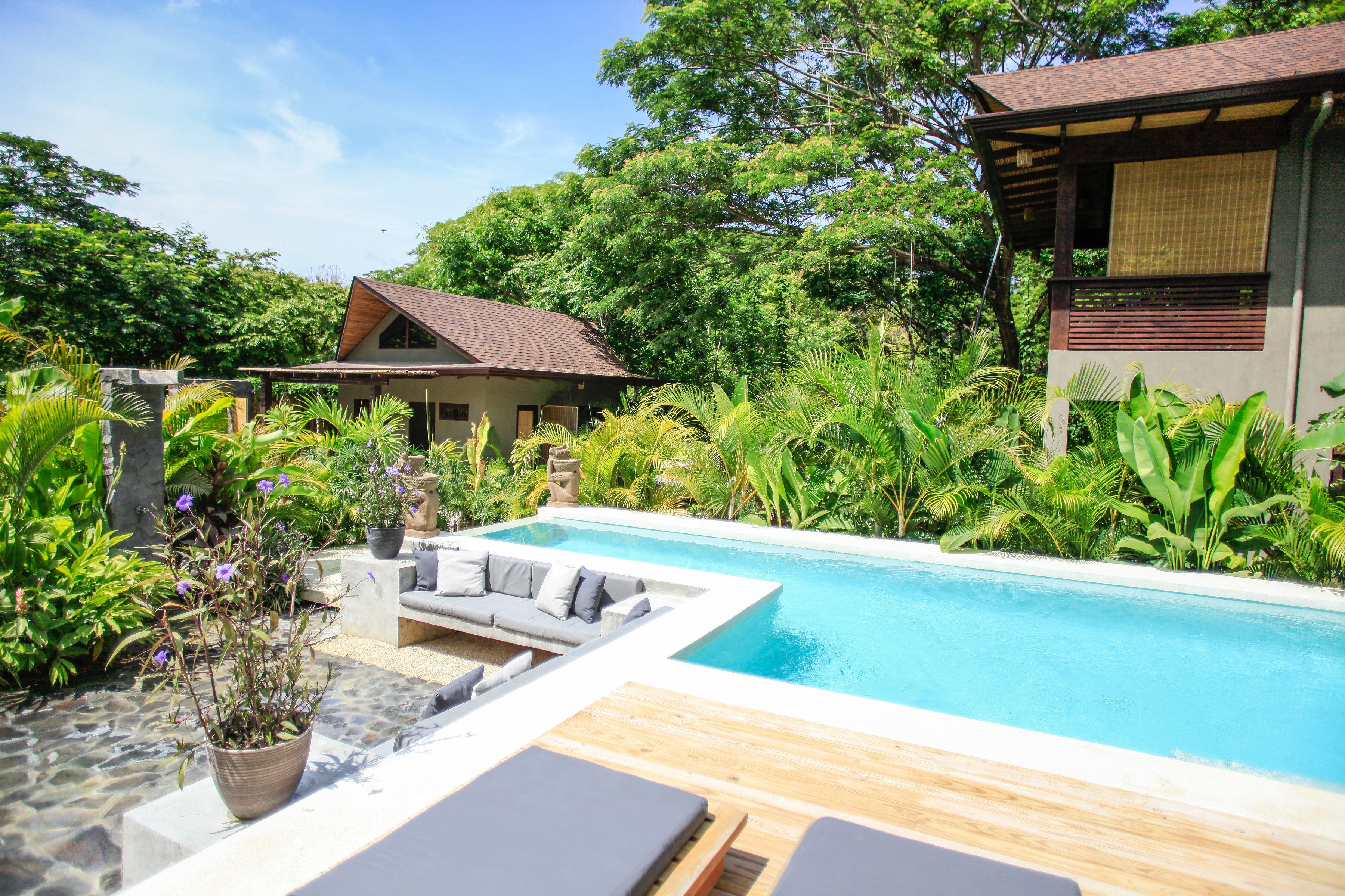 A pool area with a wooden deck, a sofa, and a stone wall.