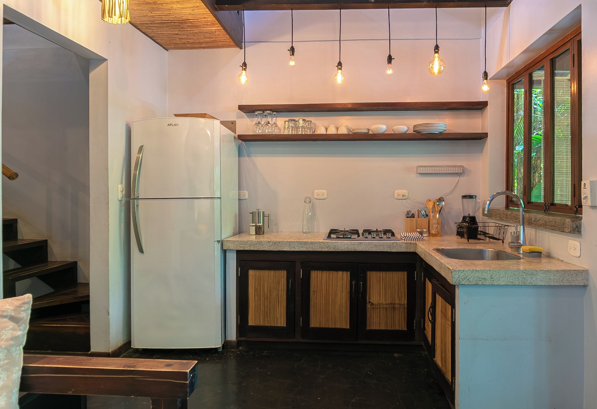 Cocina pequeña con refrigerador, estufa a gas y pileta. Hay luces colgantes sobre la encimera y una ventana con vistas.