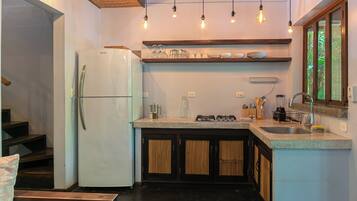 Cocina pequeña con refrigerador, estufa a gas y pileta. Hay luces colgantes sobre la encimera y una ventana con vistas.