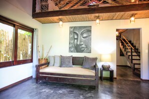A room with a wooden sofa, a wall-mounted Buddha statue, and a staircase.