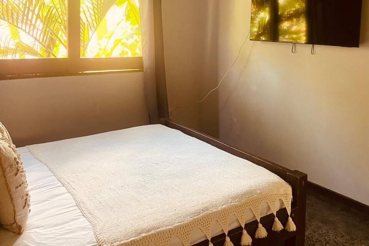 A bedroom with a bed, a window with curtains, an air conditioning unit, and a mounted television.