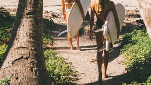 A beach scene with palm trees and two people carrying surfboards. - Lua Villas (Cóbano)