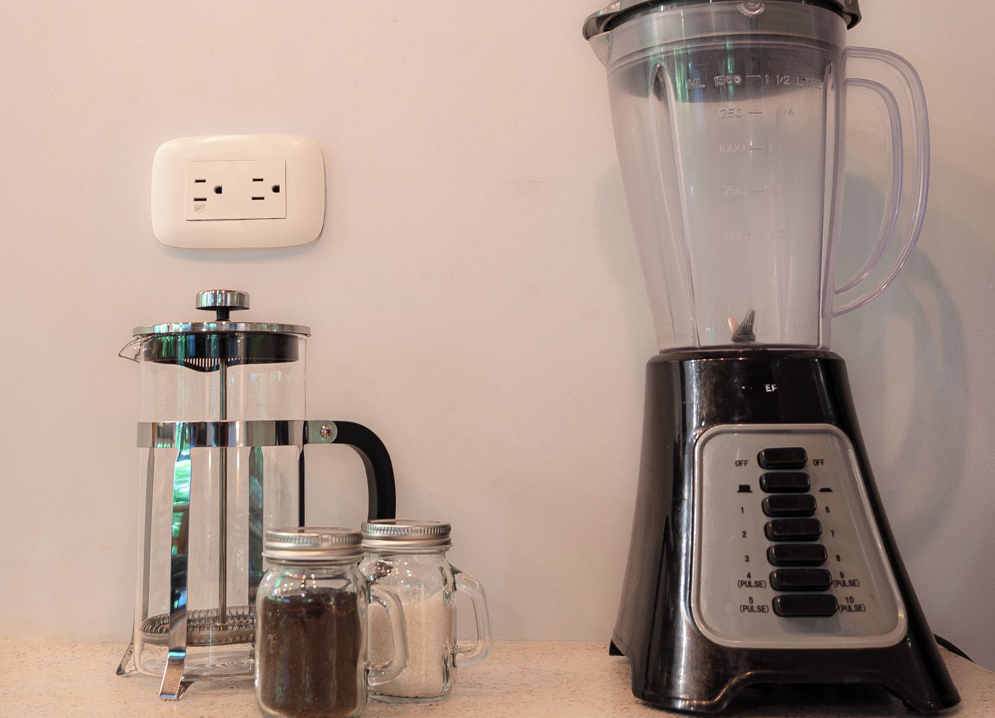 Una encimera de cocina con una licuadora, una cafetera y dos frascos de vidrio.