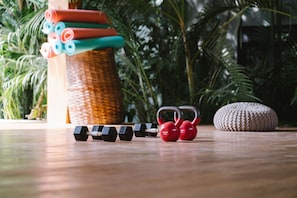Ein Holzboden mit Trainingsgeräten, darunter Kurzhanteln und Kettlebells, und ein gewebter Korb im Hintergrund.