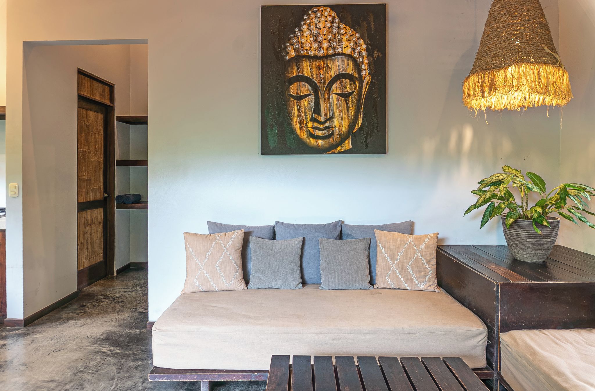 A room with a sofa, a Buddha painting, a hanging light fixture, and a potted plant.