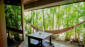 A hammock chair tied between two windows, a table with two glasses and a bottle, and lush green foliage outside. - Lua Villas (Cóbano)